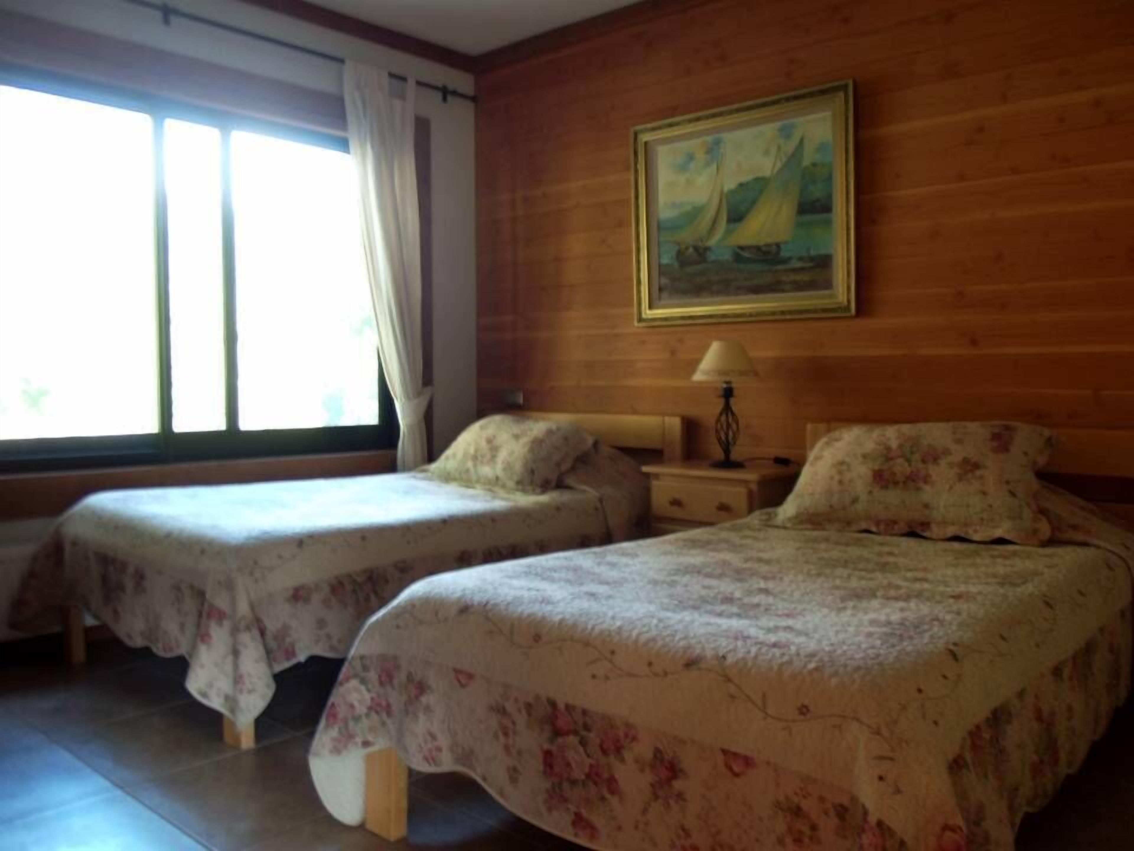 A room with two beds, a painting on the wall, and a window with curtains.