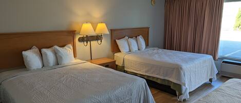 A hotel room with two beds, each with white bedding and headboards, a nightstand with lamps, and a window with curtains.