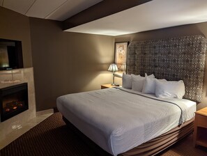 A hotel room with a large bed, a fireplace, a nightstand, and a wall-mounted TV.