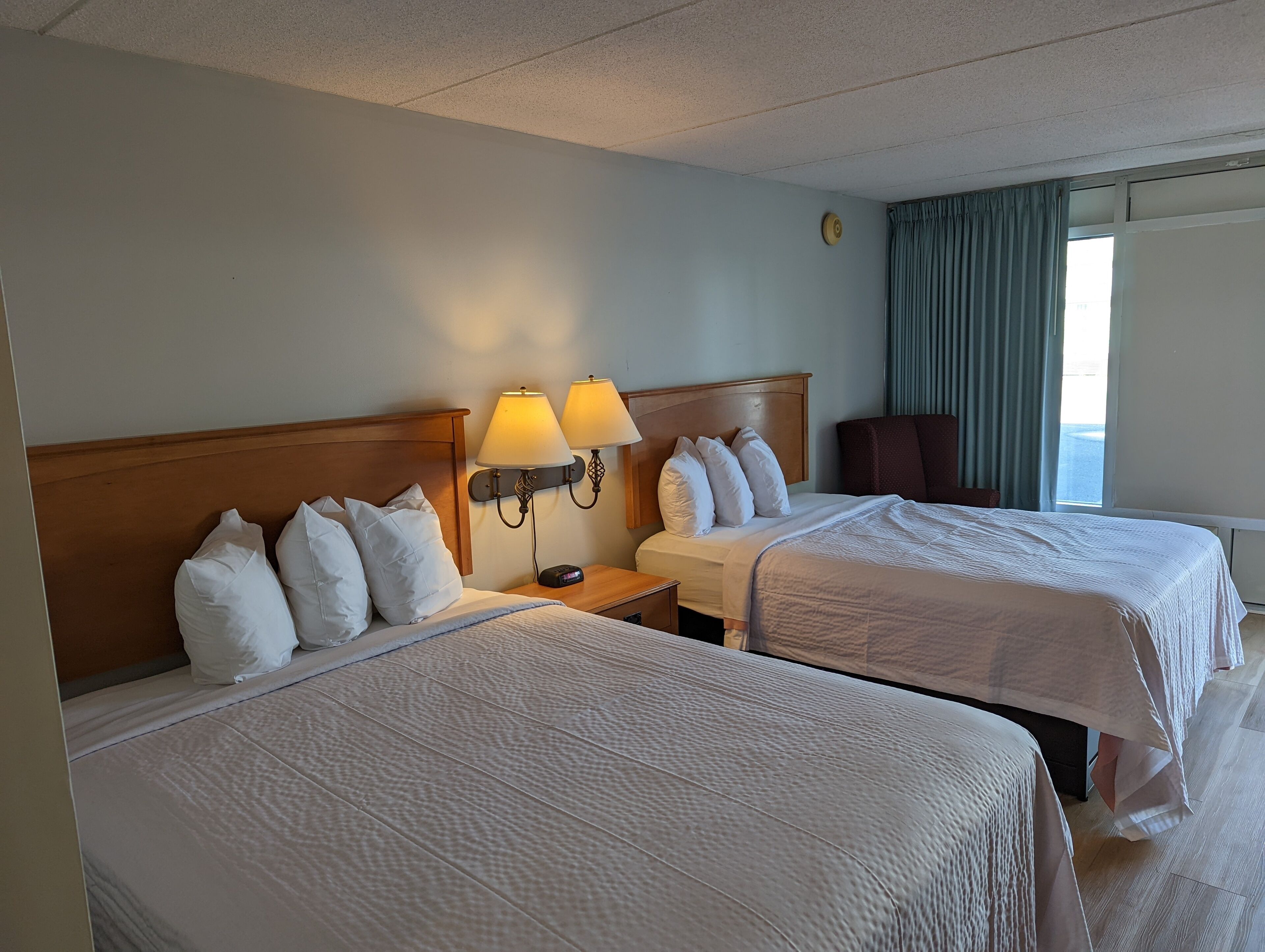 Een hotelkamer met twee bedden, elk voorzien van witte beddengoed en kussens, een houten hoofdbord en twee wandlampen.