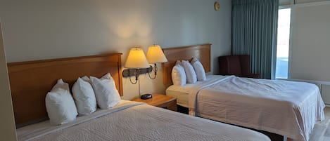 Een hotelkamer met twee bedden, elk voorzien van witte beddengoed en kussens, een houten hoofdbord en twee wandlampen.