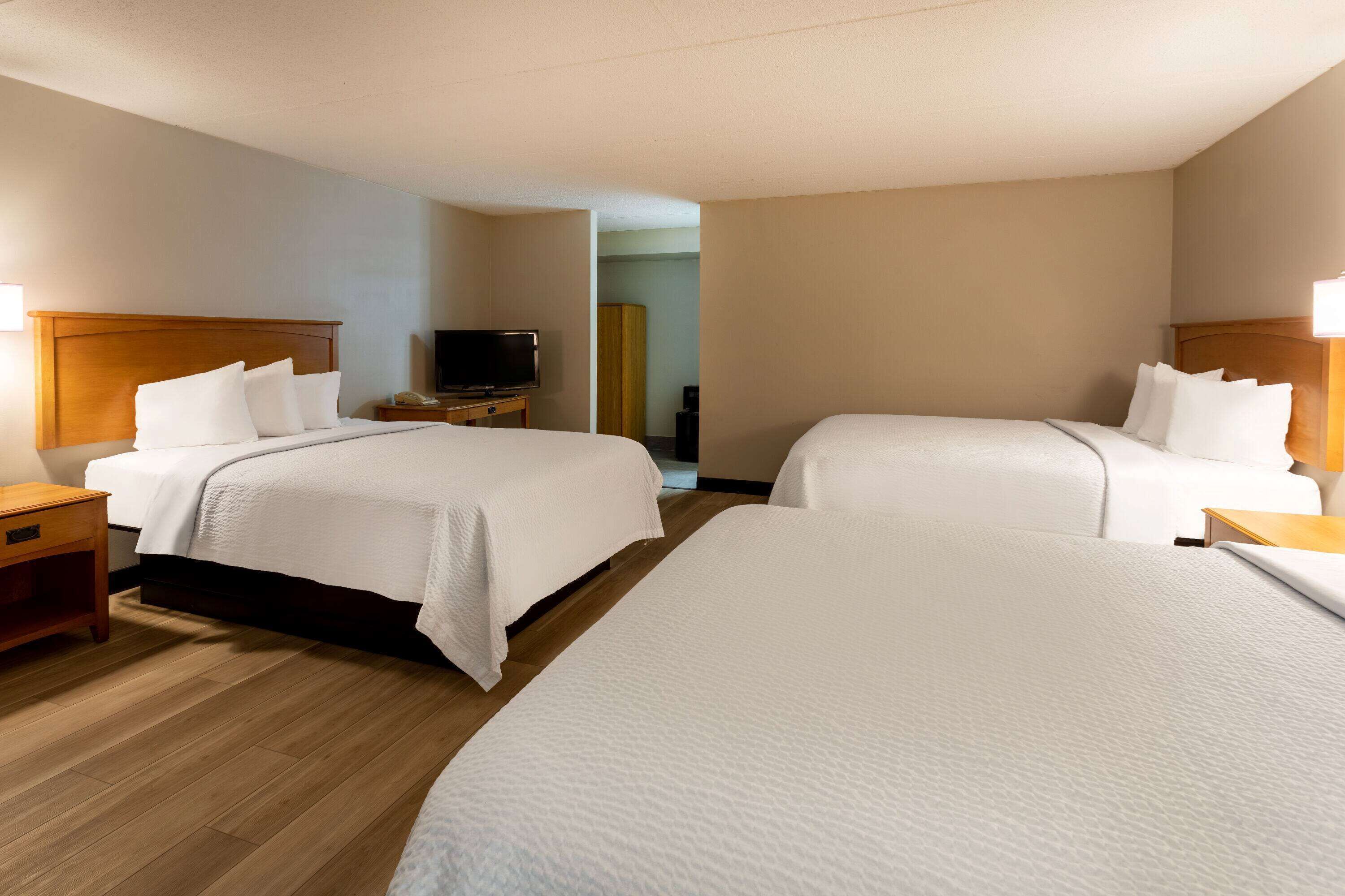 A hotel room with two beds, wooden flooring, a television on a nightstand, and a closet in the background.