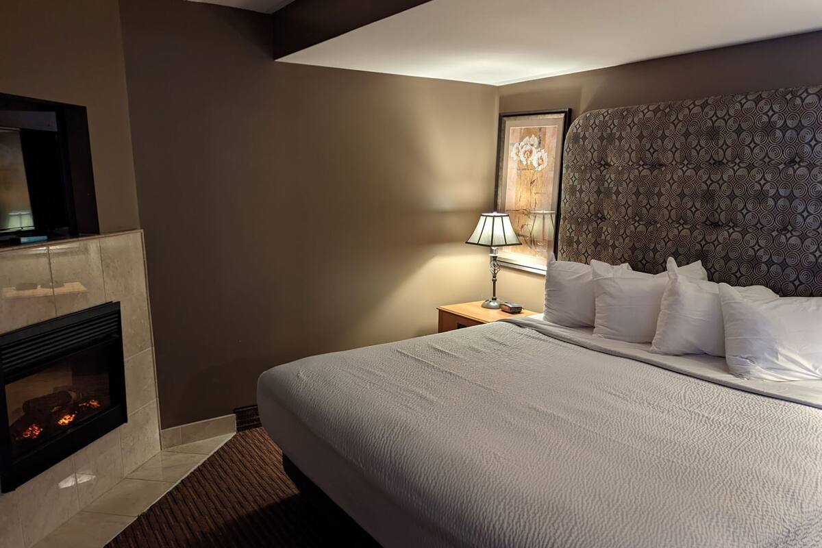 A hotel room with a bed, a fireplace, a nightstand, a lamp, and a wall-mounted TV.