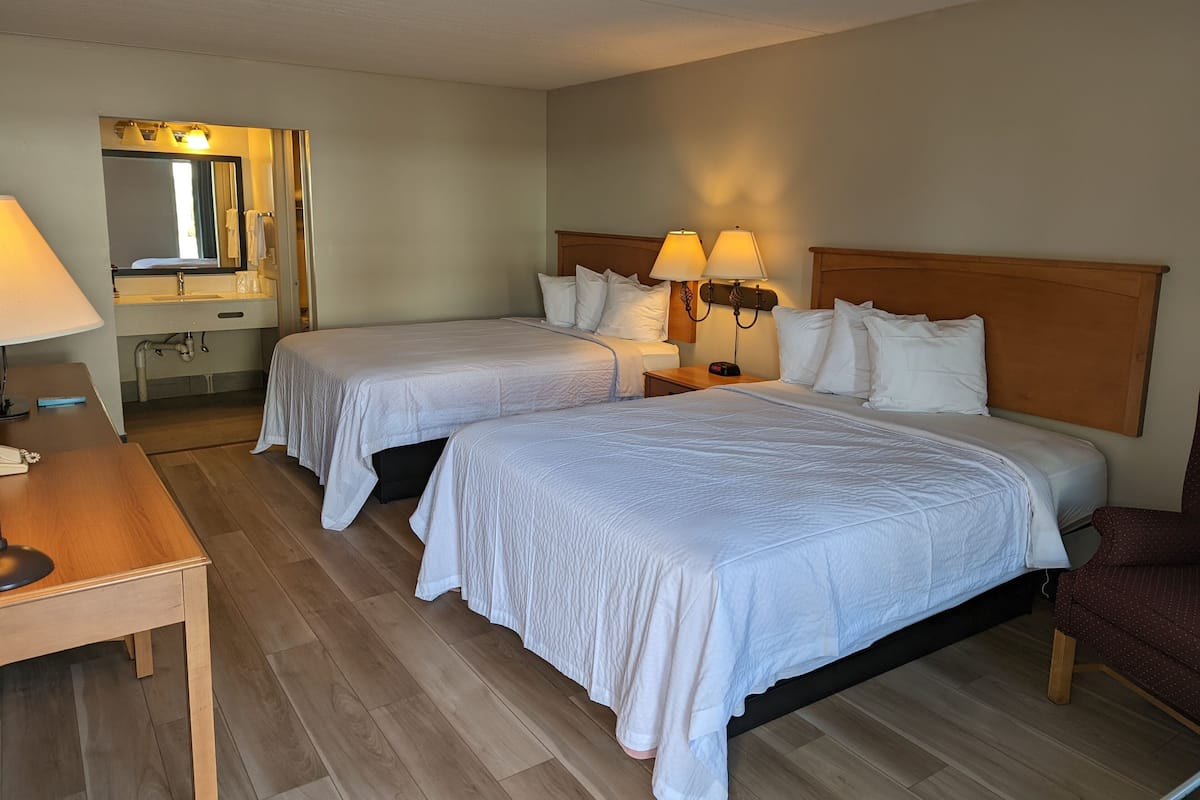 A hotel room with two beds, a wooden desk, a mirror, and a nightstand with lamps.