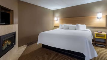 Habitación de hotel con una cama grande, televisión montada en la pared, chimenea y mesita de noche con un reloj.