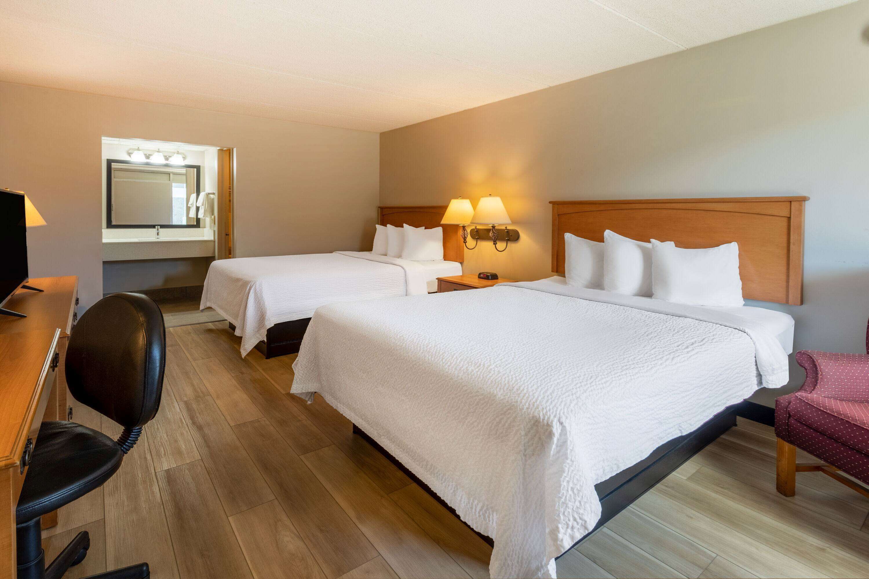 A hotel room with two beds, a desk with a chair, a mirror, and a nightstand with lamps.