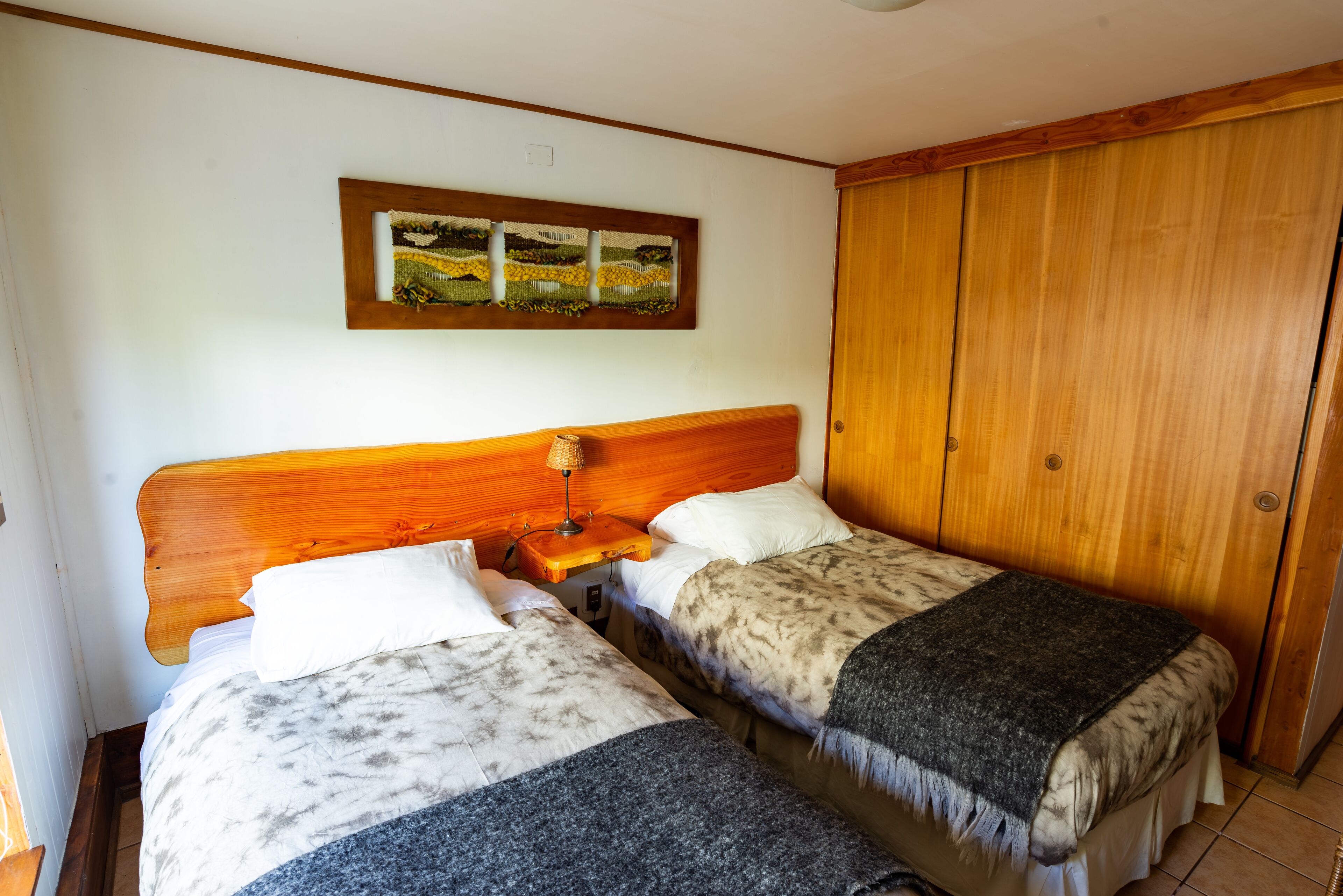 A room with two beds, wooden headboards, a wooden wardrobe, and a framed artwork on the wall.