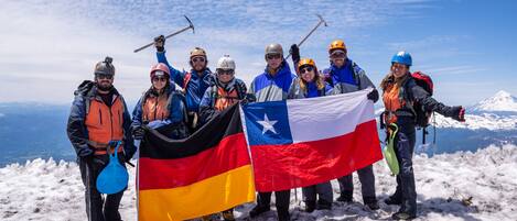 Un grupo de personas en una montaña nevada con banderas, usando cascos y cargando mochilas.