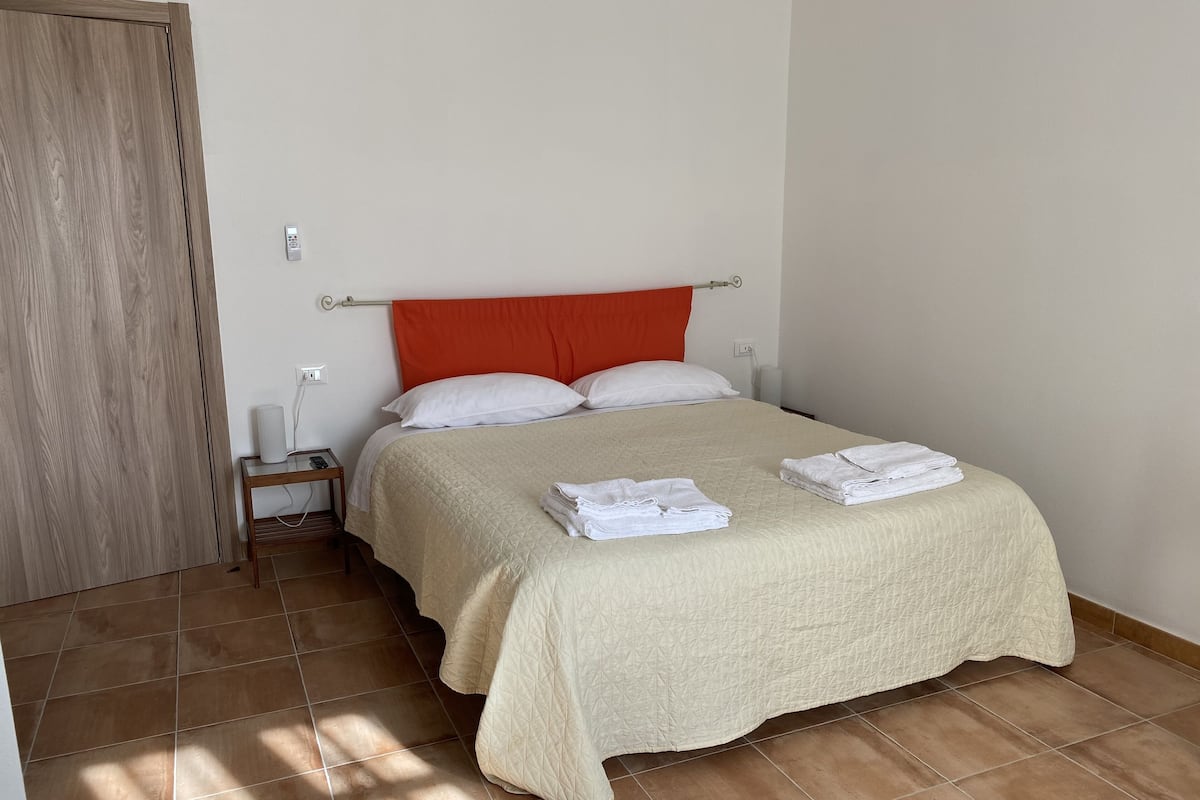 Un lit bien fait, recouvert d’une courtepointe beige, avec deux oreillers blancs et des serviettes blanches pliées posées sur le lit.