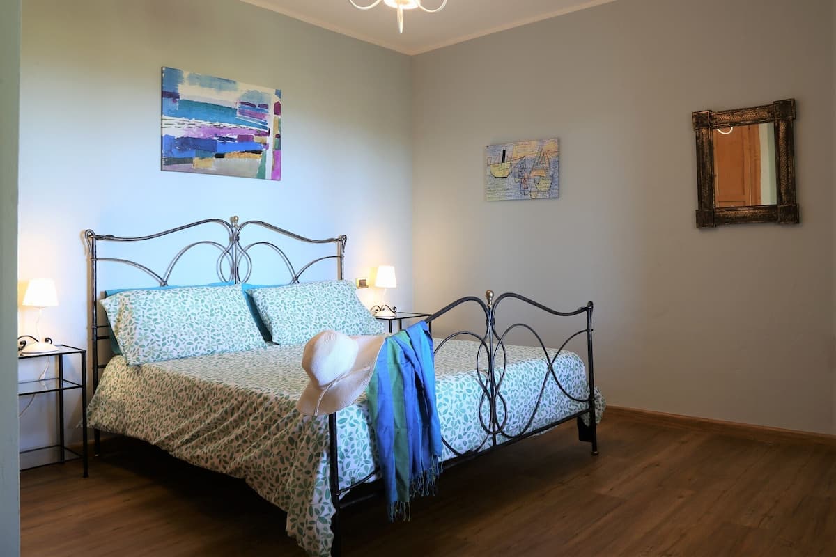 A bedroom with a metal bed frame, a patterned bedspread, two wall-mounted lamps, and a ceiling light fixture.