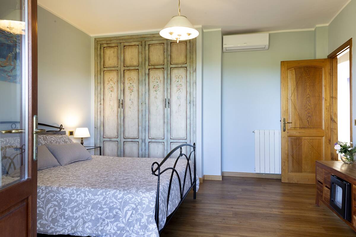 A bedroom with a bed, wooden wardrobe, and a small table with a lamp.