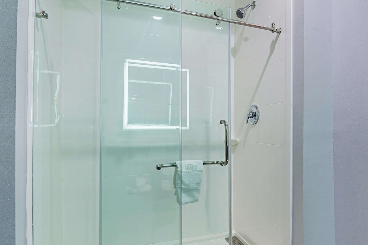 Een douche met glazen wanden, een handdouche, een handdoekhouder en een zichtbare afvoer.