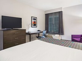 Habitación de hotel con cama, escritorio con computadora, silla, televisor y ventana con cortinas estampadas.