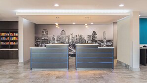 Zona de recepción con un mural de la ciudad, dos mostradores de atención al cliente y un estante con aperitivos.