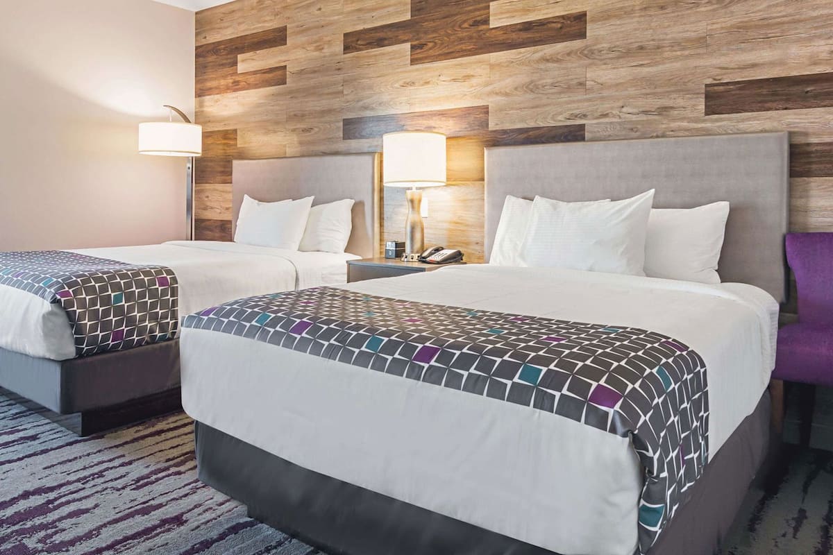 Een hotelkamer met twee bedden, een houten hoofdbord, bedlampen, een telefoon en een paarse stoel.