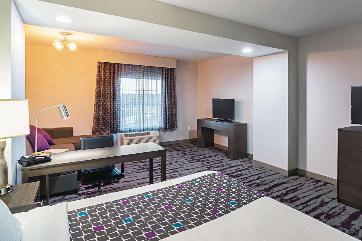 Een hotelkamer met een bed, een bureau, een stoel, een televisie en een raam met gordijnen.