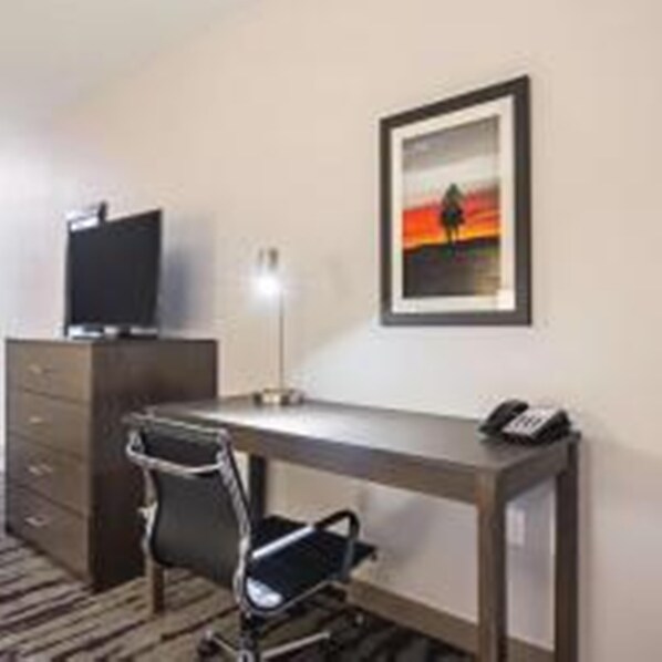 A hotel room with a desk, chair, TV, and a framed picture on the wall.