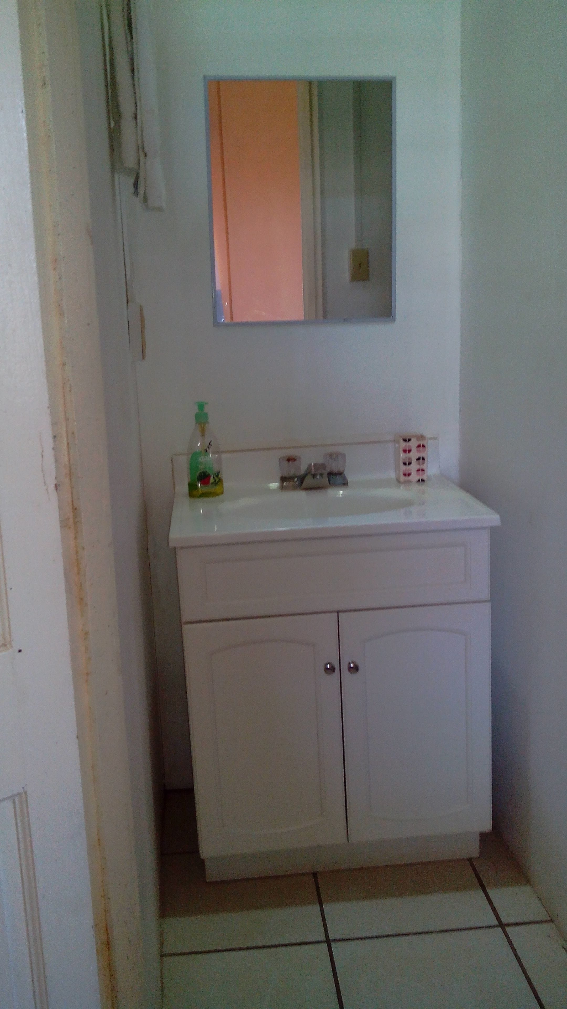 A small, white bathroom with a mirror above the sink, a toilet, and a cabinet below.