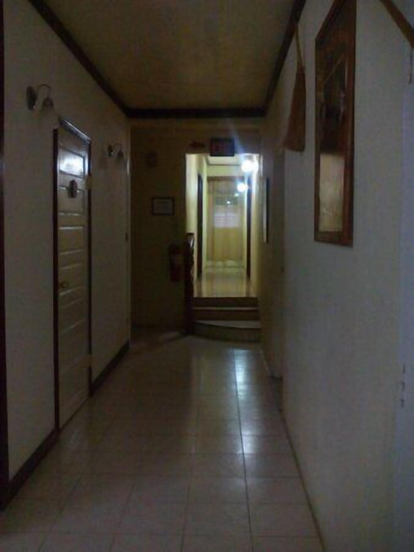 Un estrecho pasillo con suelo de baldosas, una puerta a la izquierda y una escalera que sube a un nivel superior.
