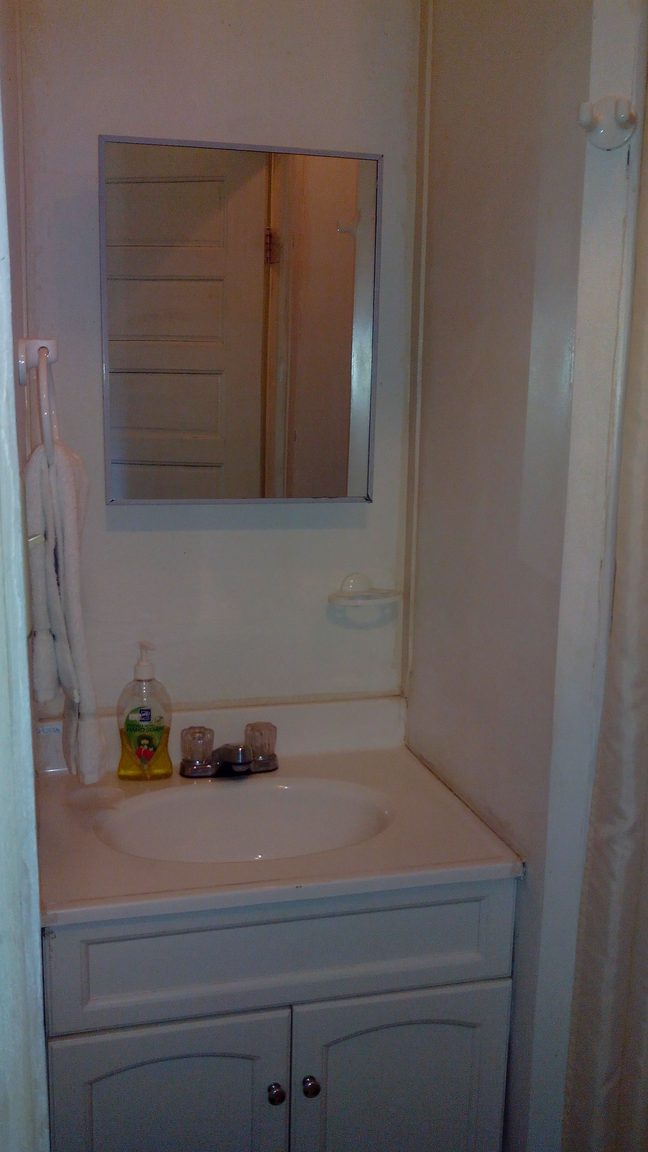 A bathroom with a white sink, a mirror, a soap dispenser, and a towel hanging on the wall.