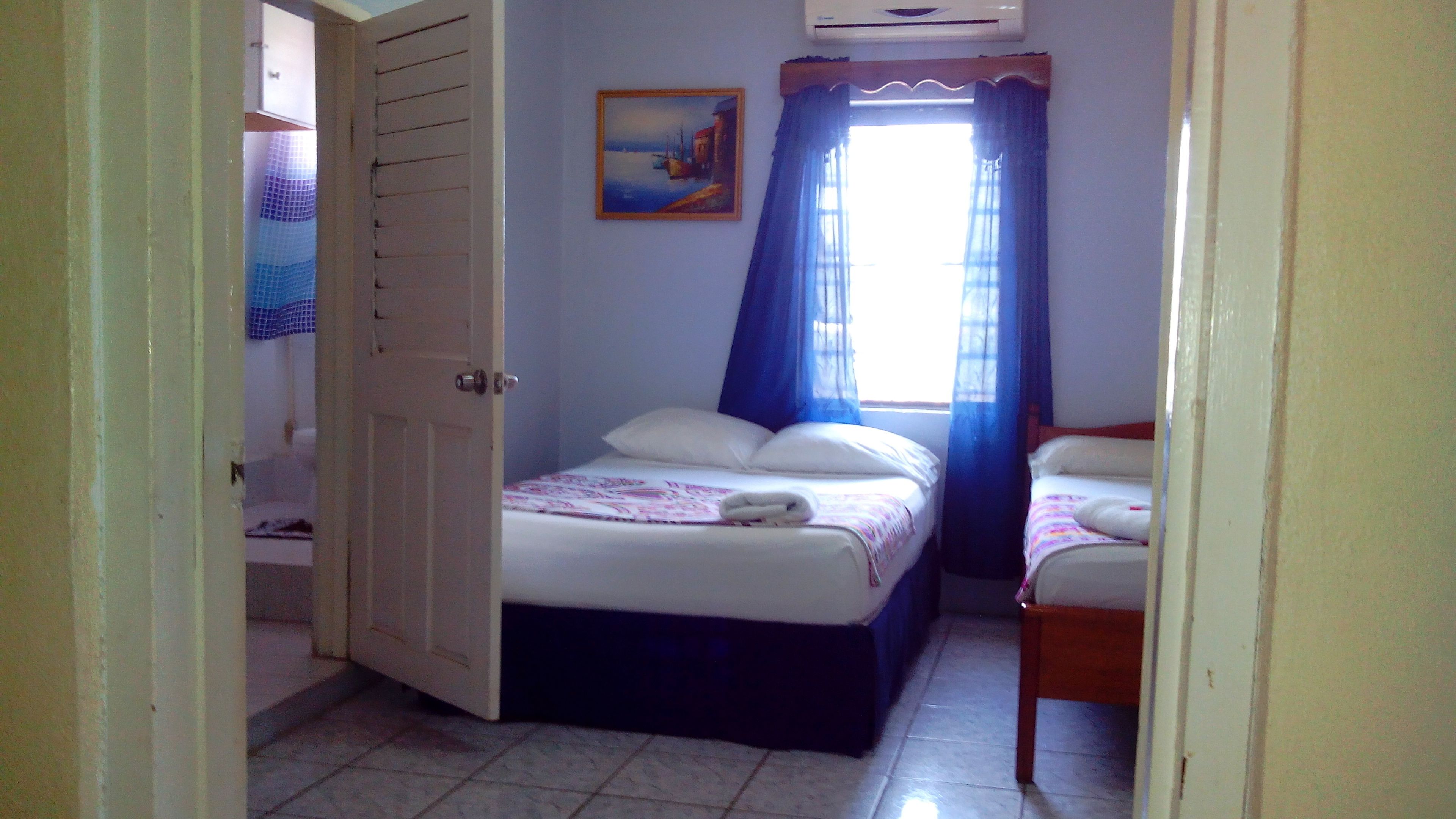 Quarto com duas camas, um quadro na parede e uma janela com cortinas.