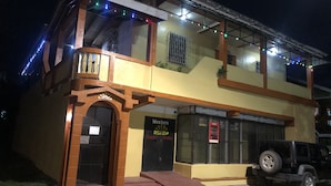 Um edifício de dois andares com varanda, um letreiro com 'Western Guest House' e um SUV preto estacionado.