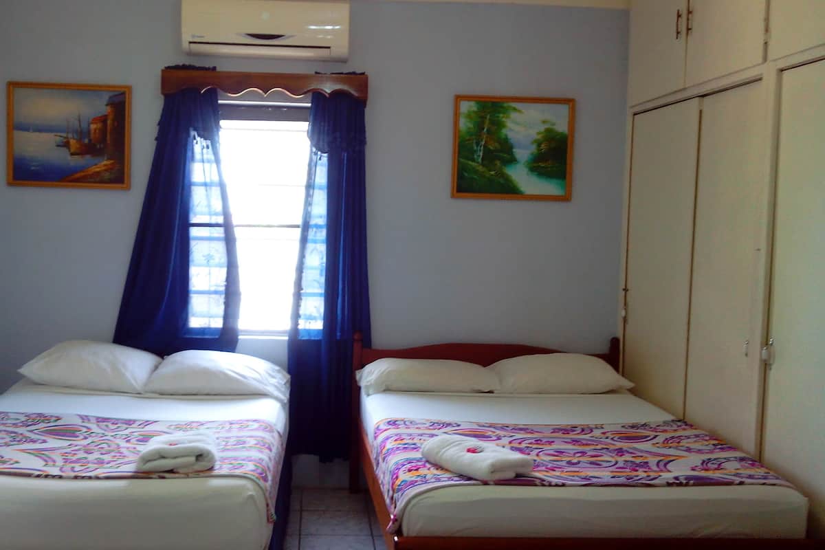A room with two beds, a window with curtains, and two paintings on the walls.