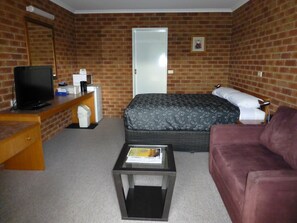 A hotel room with a brick wall, a bed with patterned bedding, a television, a desk with a computer, and a small table.