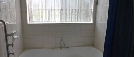 A bathroom with a bathtub, a window with a curtain, and a shower area.