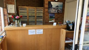 A reception desk with a clock, a framed picture, and a vase with flowers. - Inverloch Central Motor Inn (Inverloch)