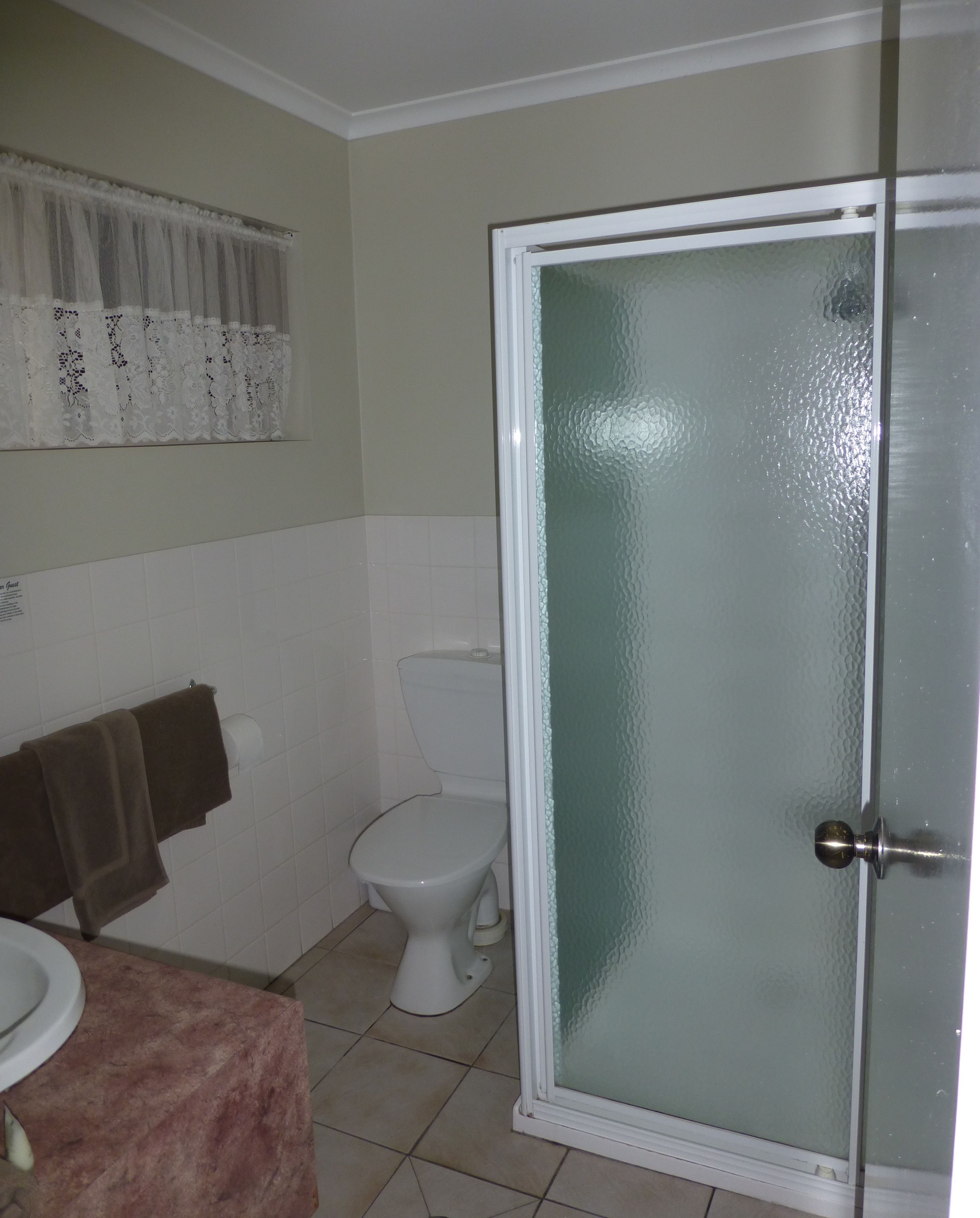 Un baño con inodoro, toallero con toallas y puerta de ducha.