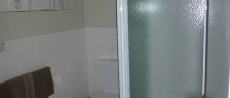 Un baño con inodoro, toallero con toallas y puerta de ducha.