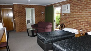 A room with two beds, a chair, a desk, and a door leading to a bathroom. - Inverloch Central Motor Inn (Inverloch)