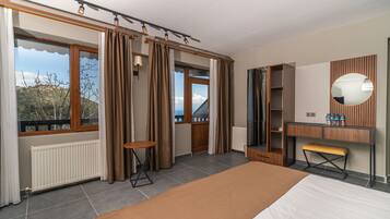 A modern bedroom with a large bed, a wooden bench, a mirror, and a view of the outdoors.