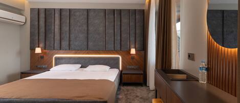 A modern hotel room with a large bed, bedside tables, a bench, a mirror, and a water bottle on the nightstand.