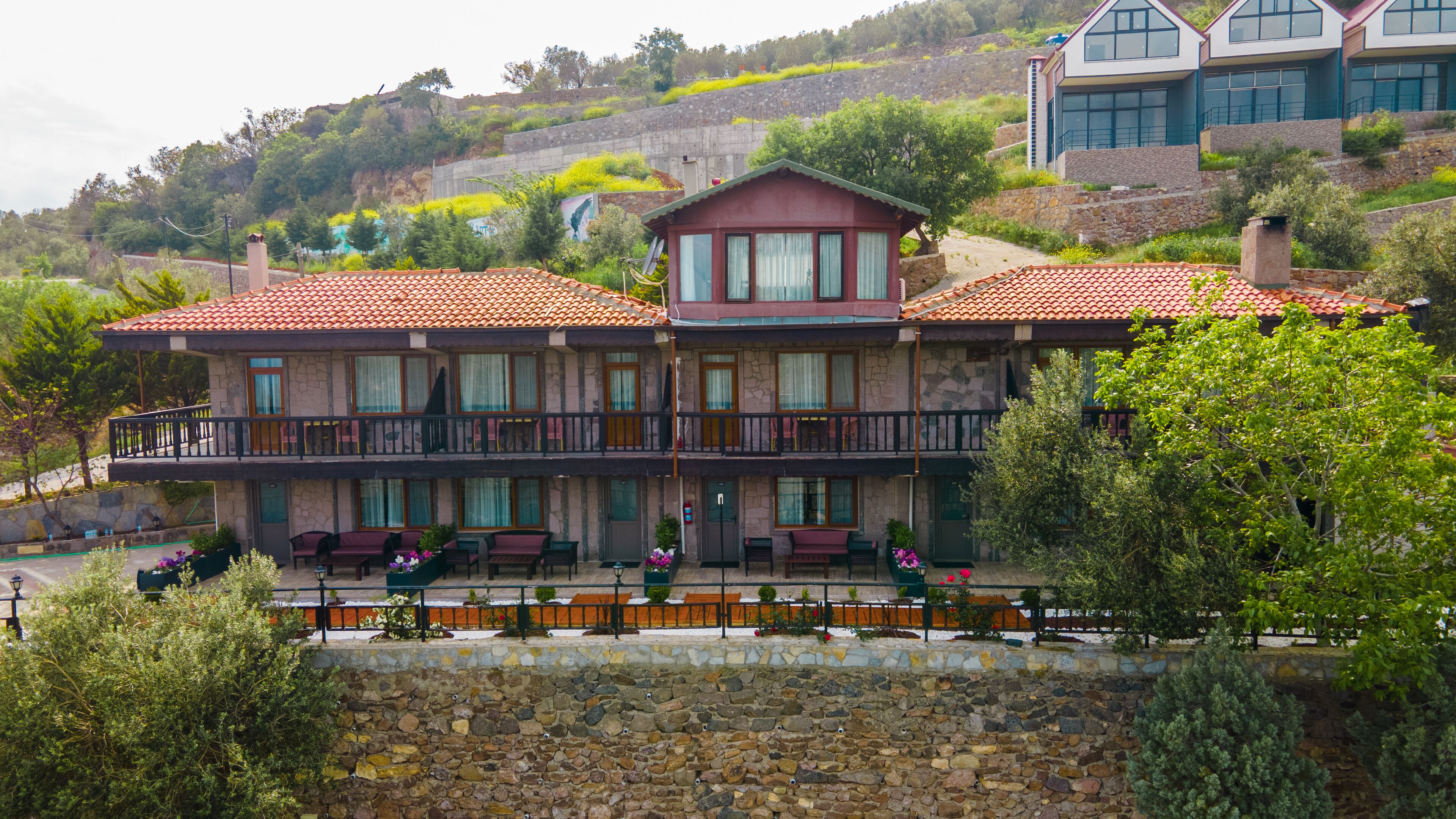 A two-story building with a red-tiled roof, stone walls, and a balcony with outdoor seating.