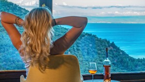 Une personne assise près d’une fenêtre, avec vue sur un paysage montagneux et un plan d’eau.
