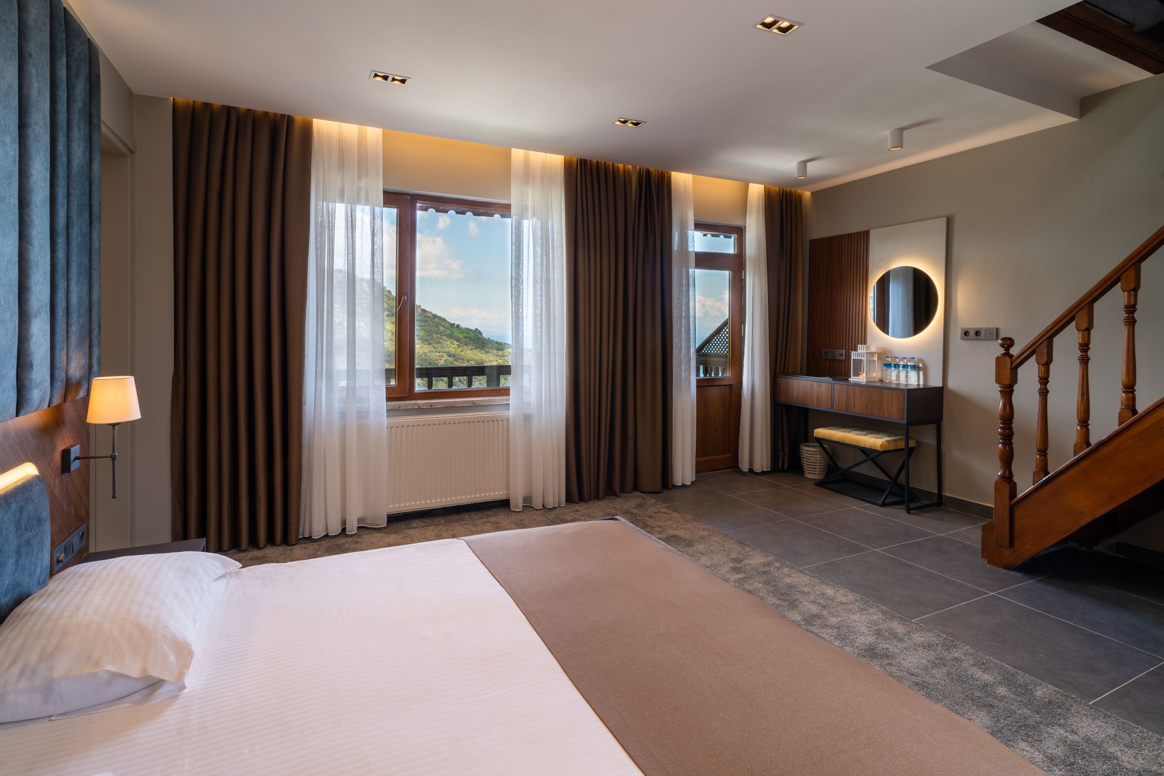 Habitación de hotel con una cama grande, un escritorio de madera, un espejo y vistas al exterior.