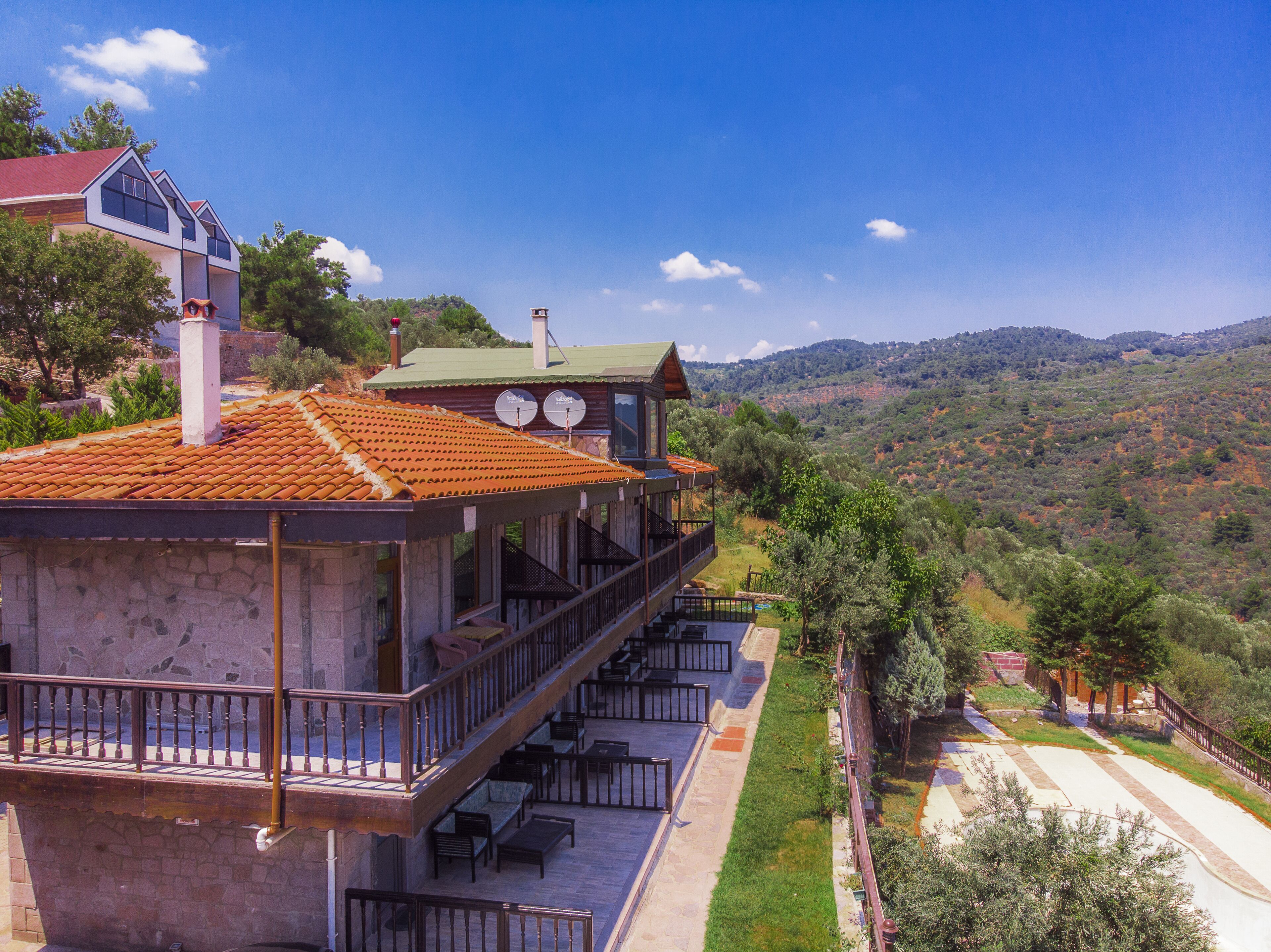 A two-story building with a balcony and outdoor seating area, surrounded by a hilly landscape.