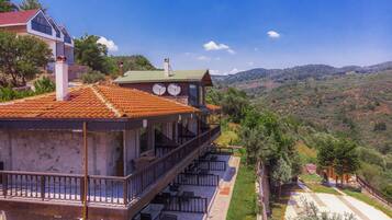 A two-story building with a balcony and outdoor seating area, surrounded by a hilly landscape.
