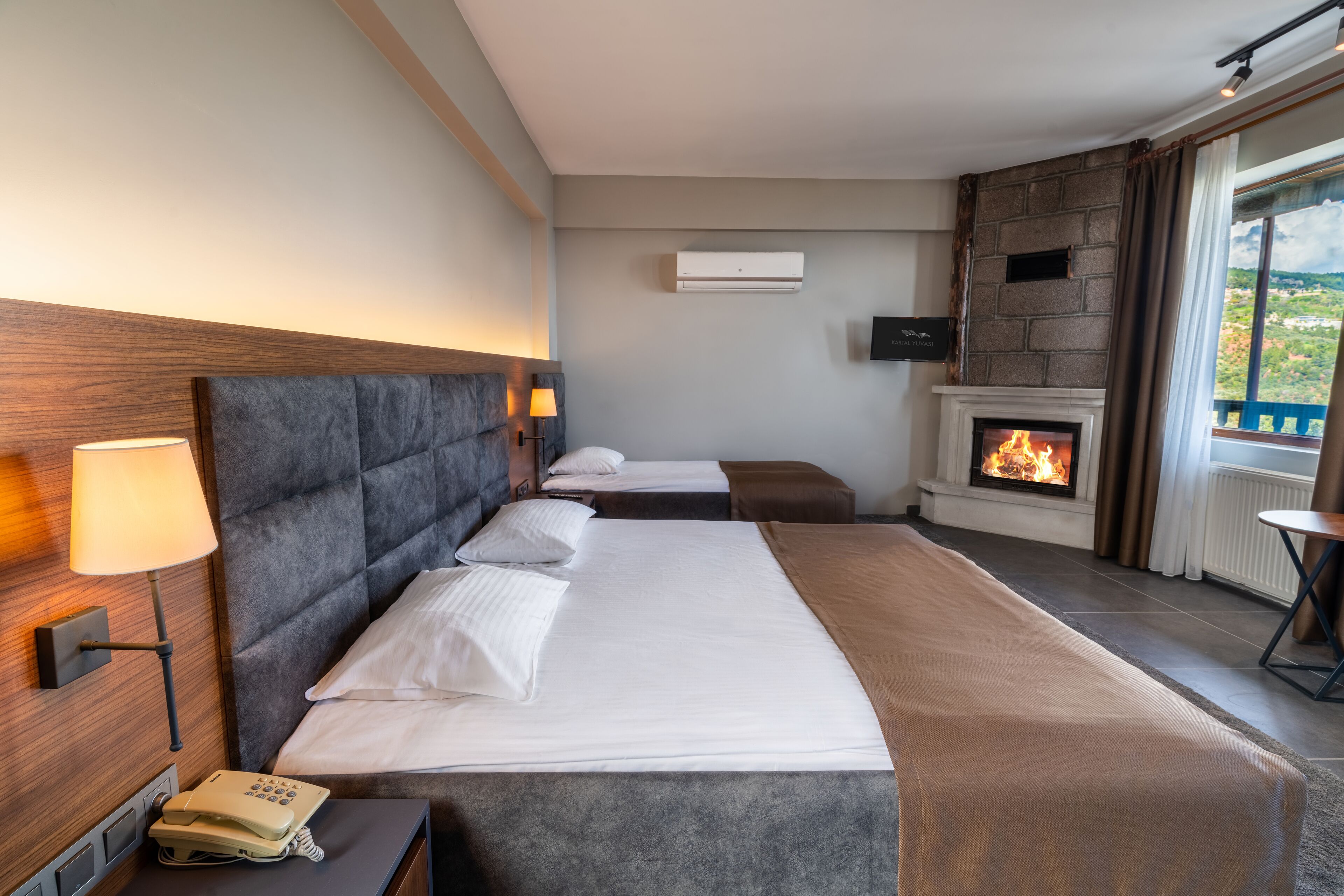 Habitación de hotel con una cama grande, un teléfono en la mesita de noche, un televisor montado en la pared y una chimenea.