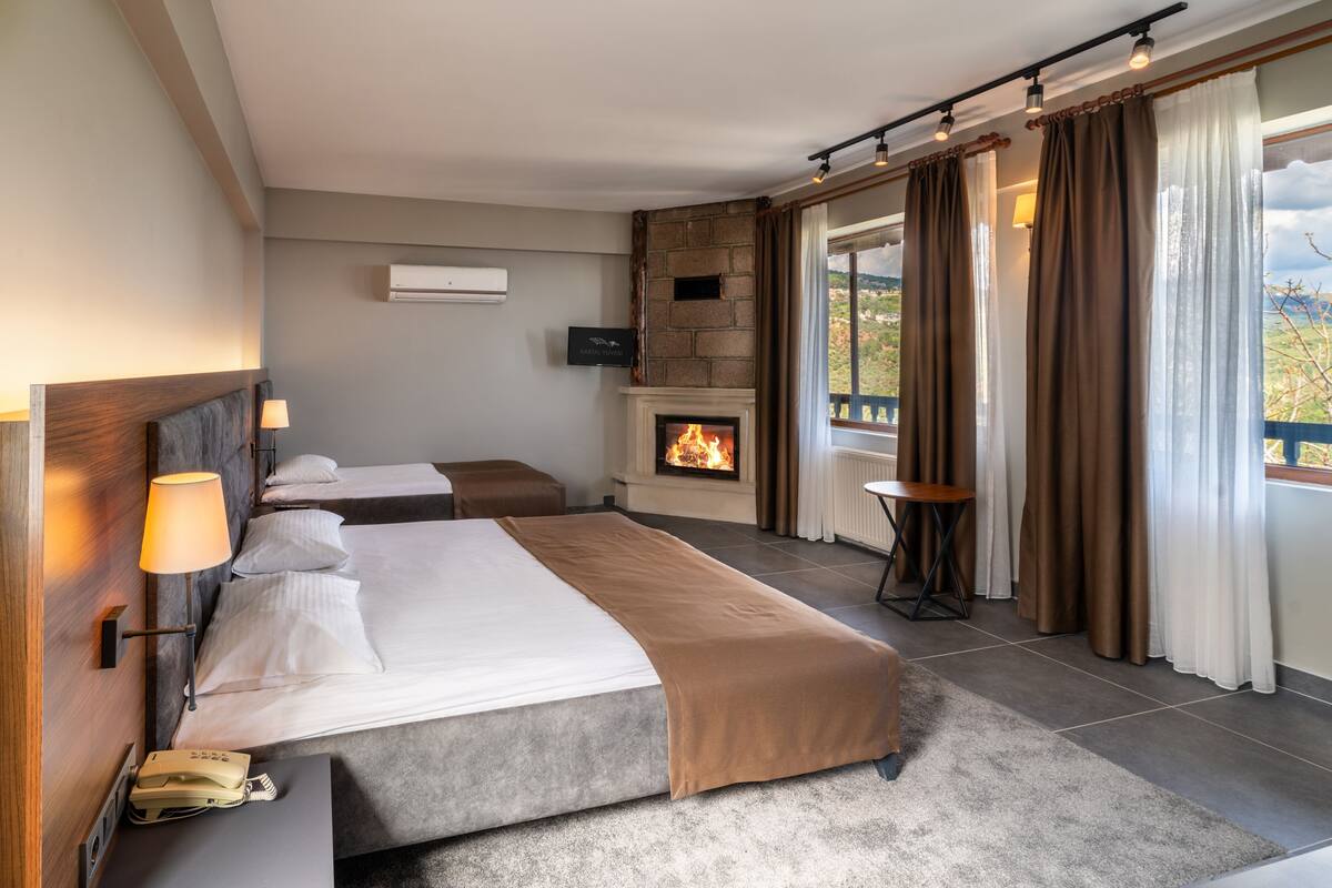 Une chambre d’hôtel avec une cheminée, deux lits, une petite table et une vue sur l’extérieur.