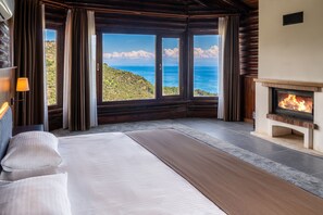 A bedroom with a large bed, a fireplace, and a view of the sea. - Assos Kartal Yuvası Boutique Hotel (Ayvacik)