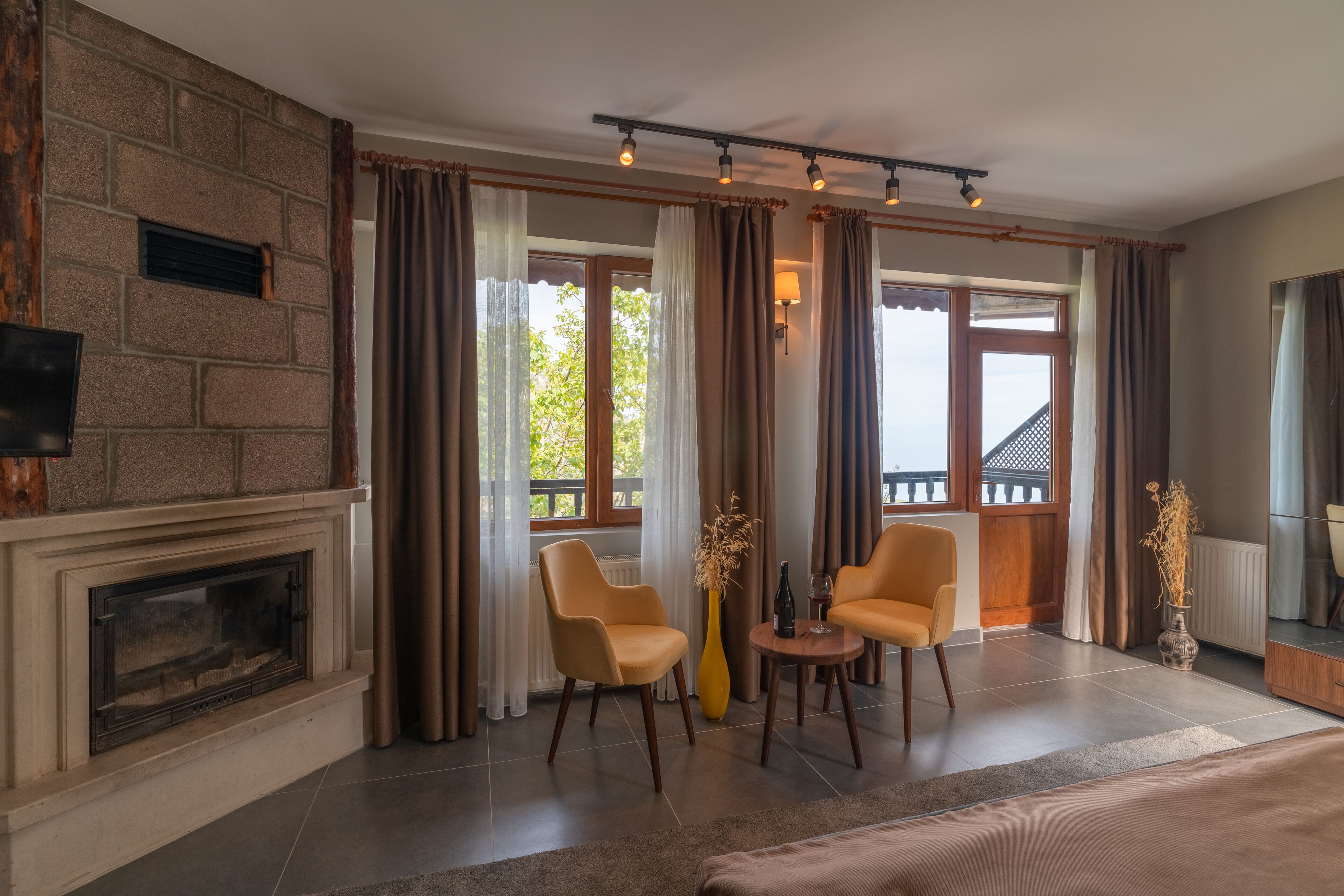 Una sala de estar moderna con chimenea, dos sillones, una mesa de centro y ventanas amplias con cortinas.