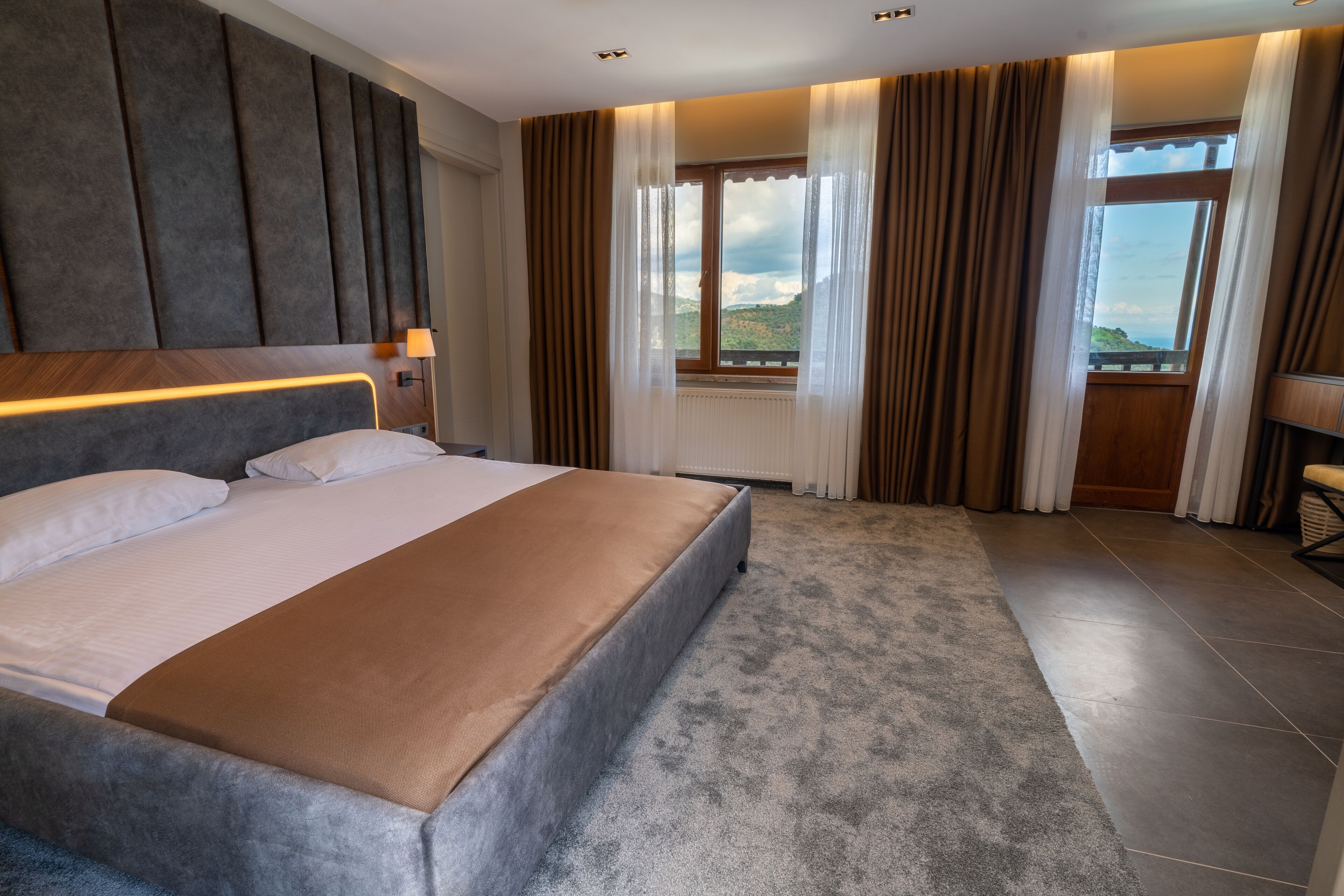 A modern hotel room with a large bed, a view of the mountains, and a window with curtains.