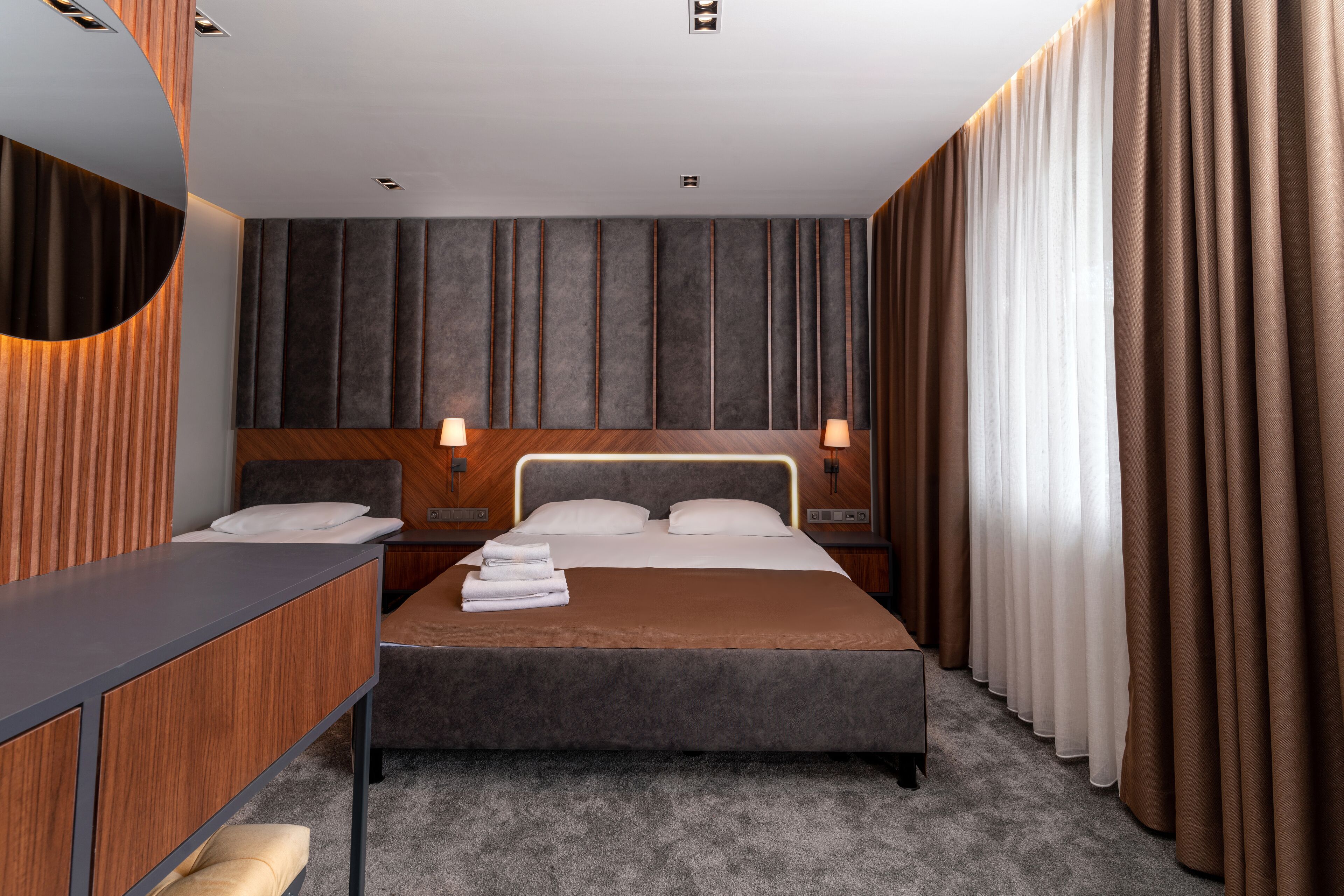Moderni hotellihuone, jossa on suuri sänky, työpöytä ja peili.