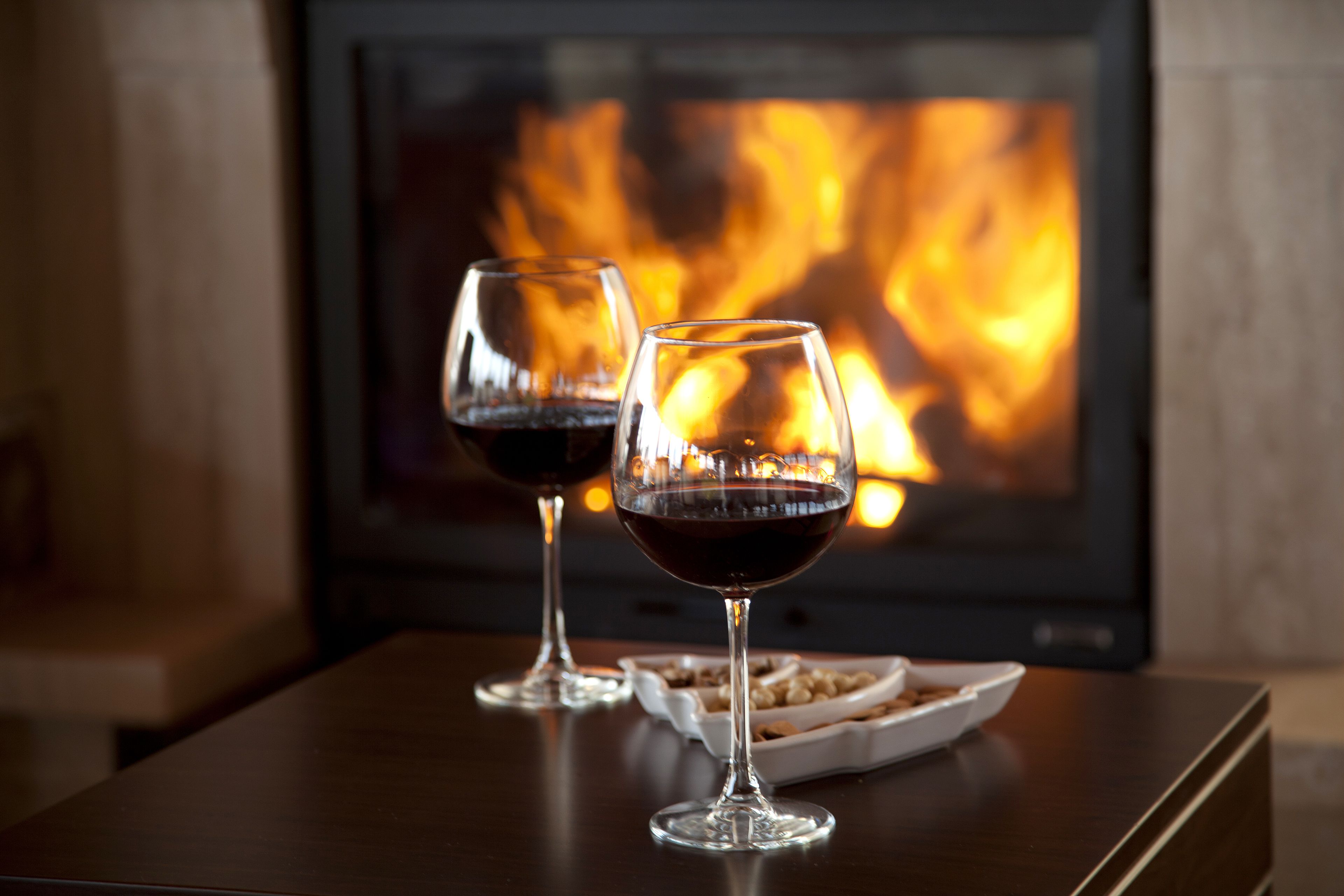 Dos copas de vino sobre una mesa, con una chimenea al fondo.