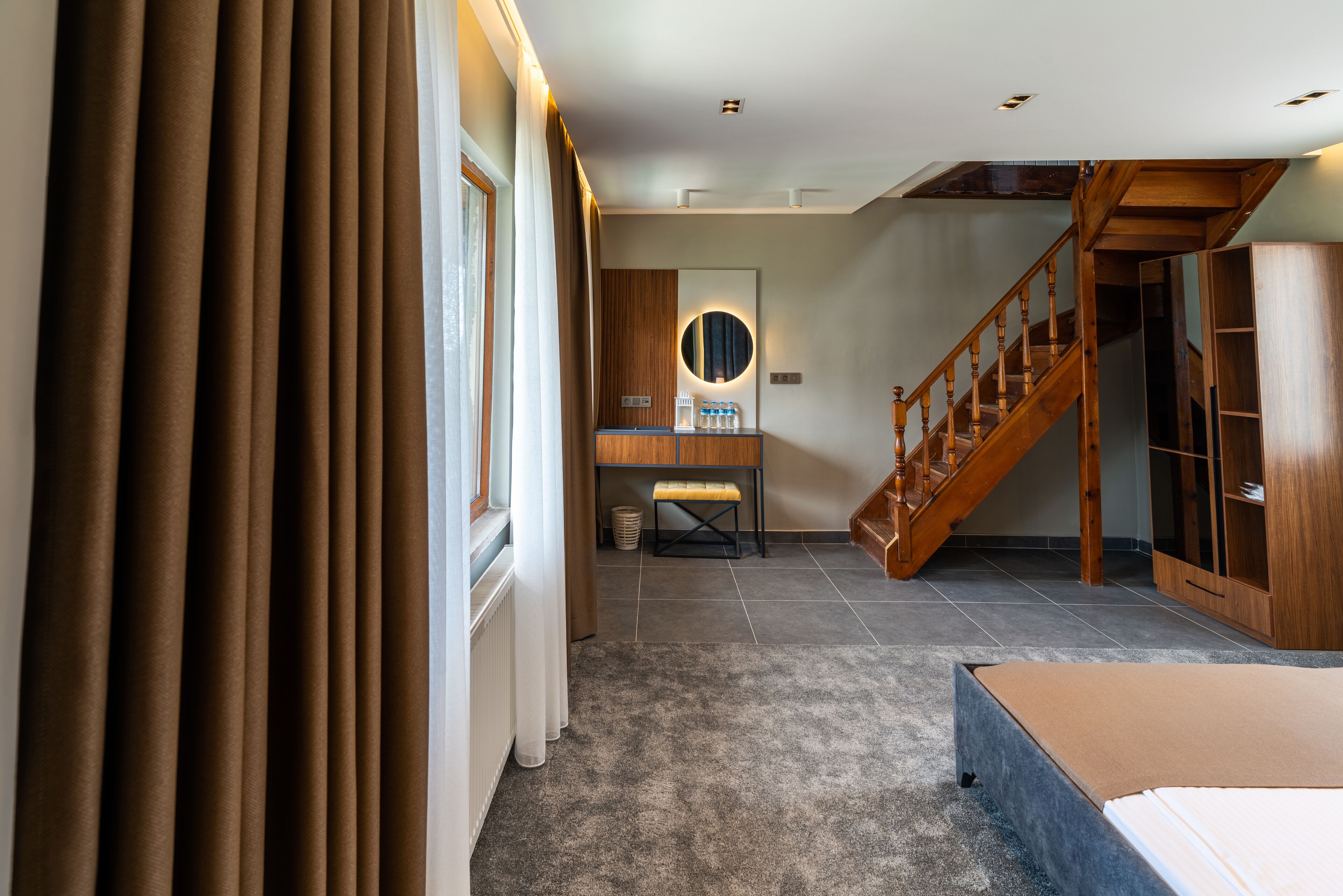 A hotel room with a wooden staircase, a round mirror, a small bench, and a bed.