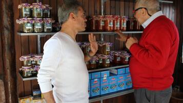 Two men in a rustic setting with shelves stocked with jars and boxes, likely a store or market.