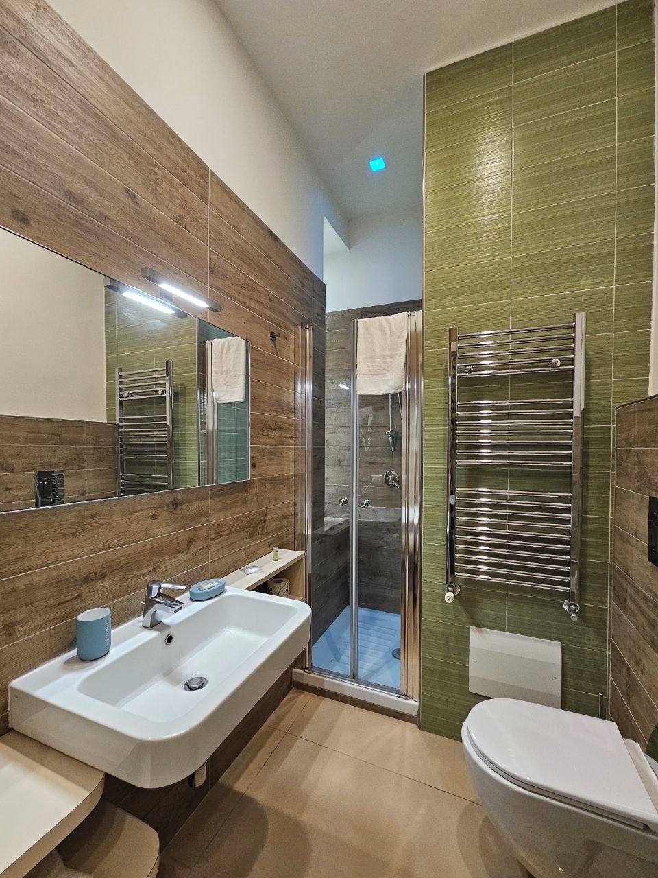 A modern bathroom with a large mirror, a sink, a toilet, and a glass-enclosed shower.